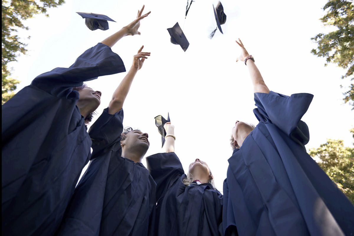 Fresno State graduates celebrate with their caps raised in the air.