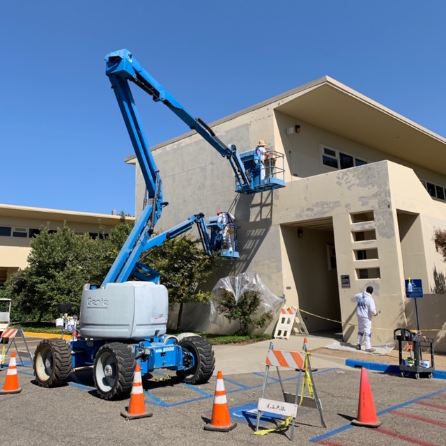 Painters working on a crane lift outside a building