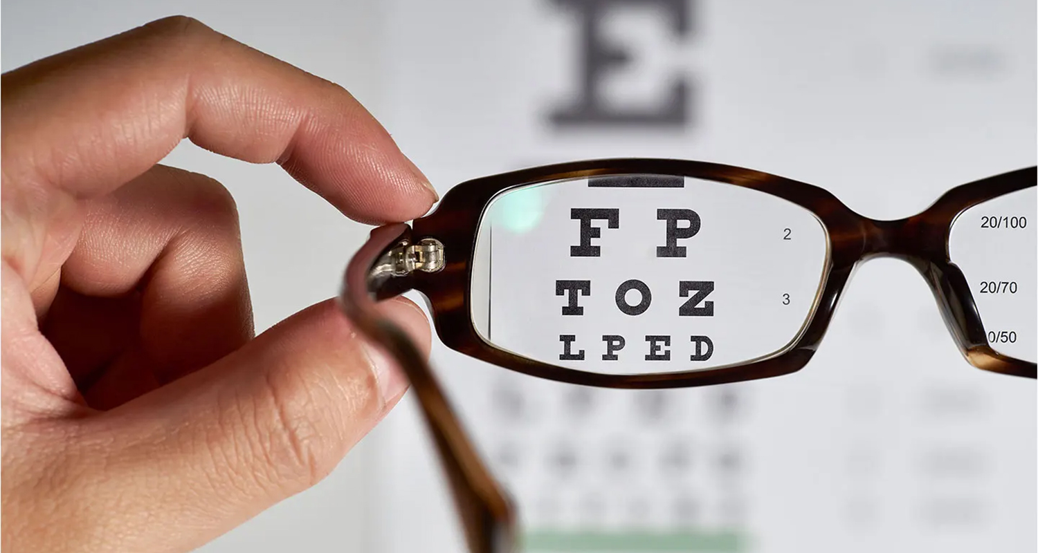 A Hand holding a pair of eyeglasses to a eye exam chart